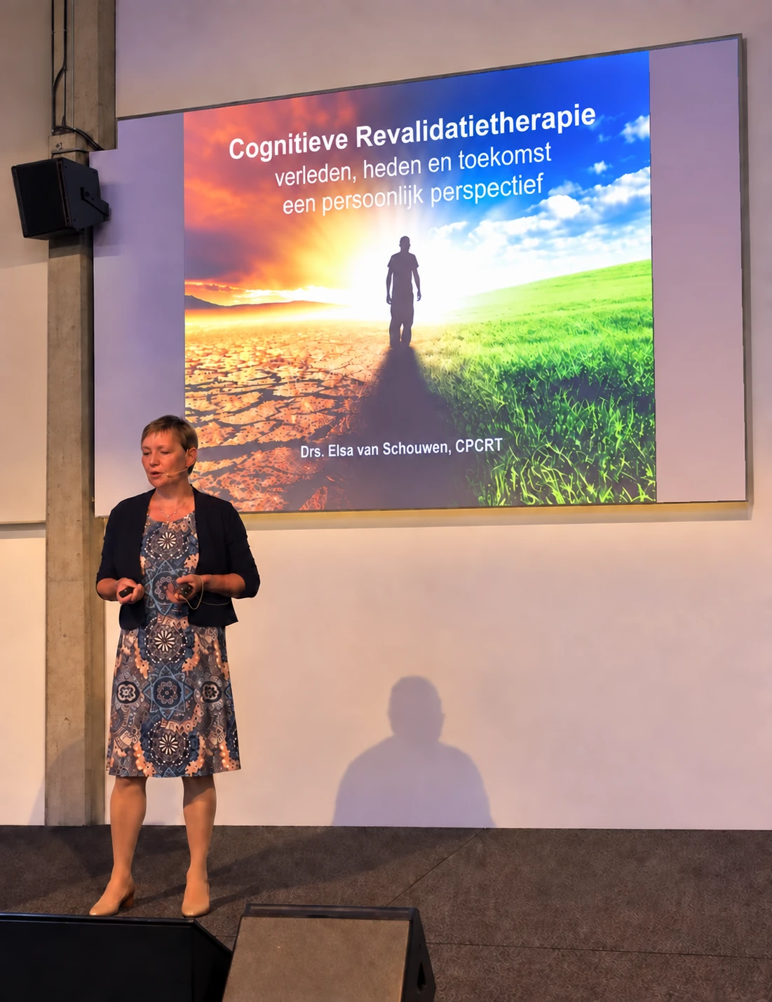 Elsa van Schouwen presenting to a room, the slide behind her reading Cognitieve Revalidatietherapie: verleden, heden en toekomst.