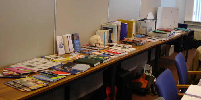 A long table laid out with books, workbooks and folders, a model skull standing among them.