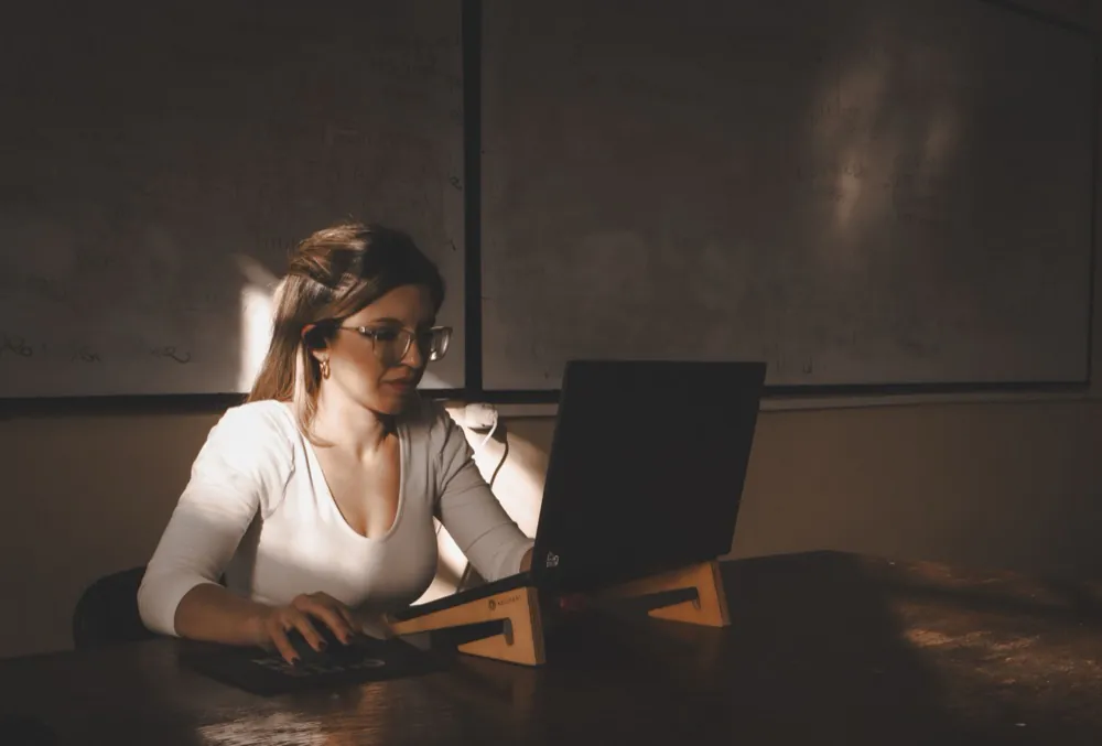 A therapist studying at a laptop in a dim classroom, lit by a shaft of afternoon sun.